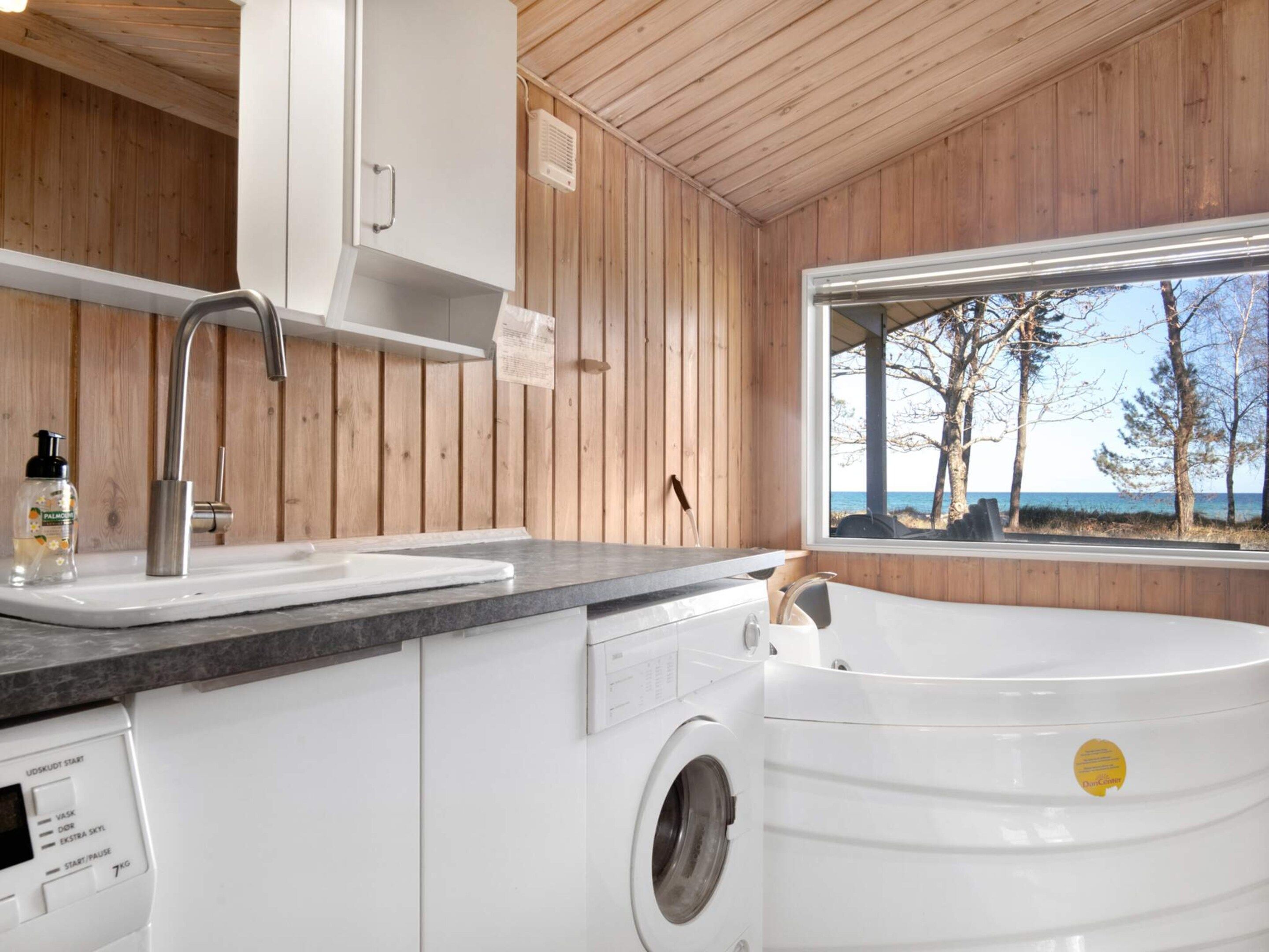 A modern kitchen with a built-in washing machine, a sink, and a window with a view of trees and the sea.
