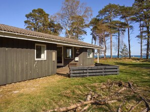 A wooden cabin with a porch, a bench, and a view of the sea. - 4 Star Holiday Home in Nexo (Nexø)