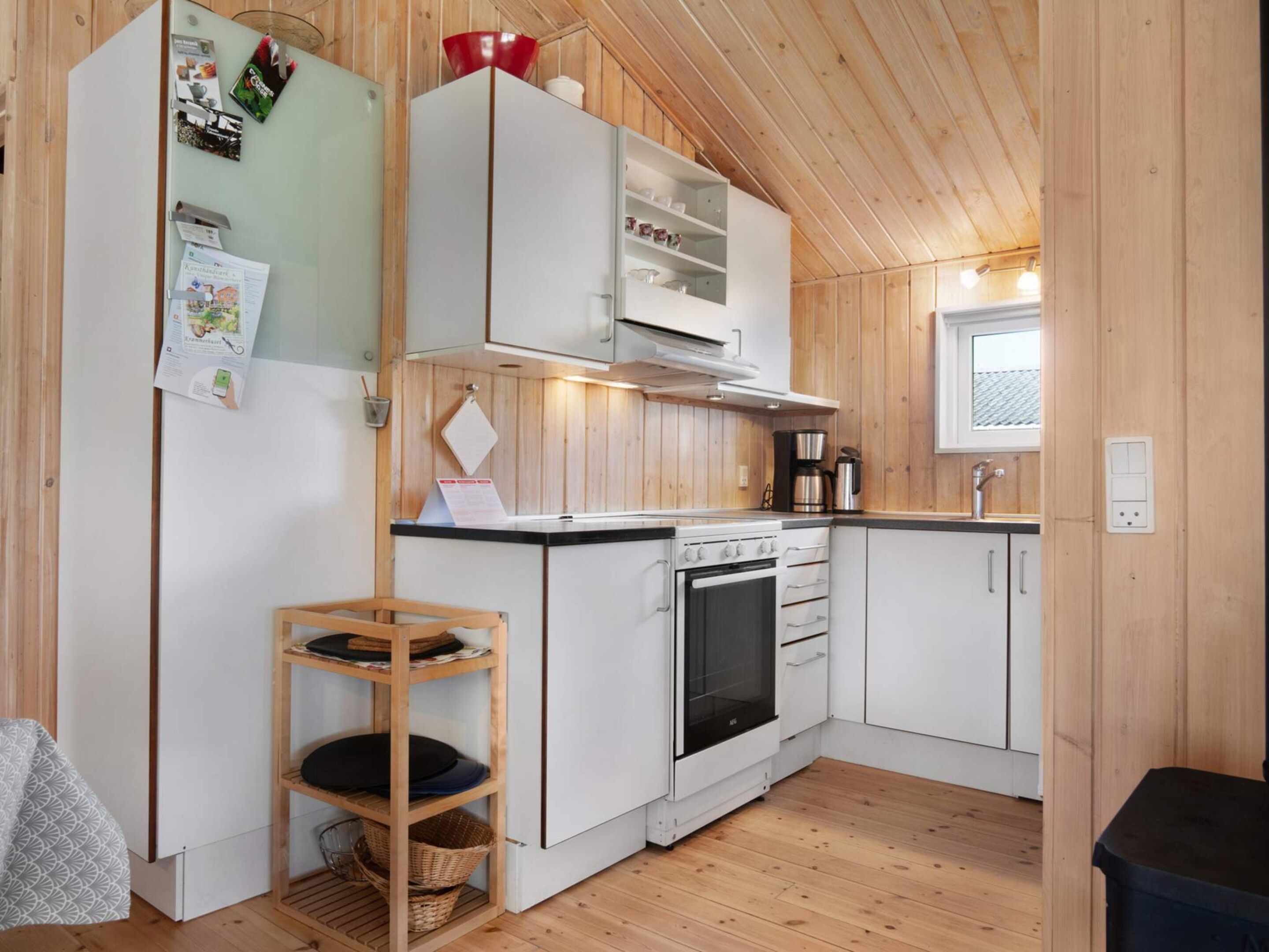 A compact kitchen with wooden walls, a white refrigerator, a stove, and a coffee maker.
