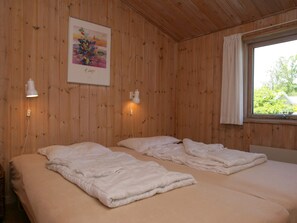 A room with wooden walls, two beds with white bedding, a painting on the wall, and a window with a view of greenery. - 4 Star Holiday Home in Nexo (Nexø)