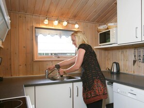 A kitchen with wooden walls, a window with curtains, a sink, a Bosch dishwasher, and a microwave. - 4 Star Holiday Home in Nexo (Nexø)