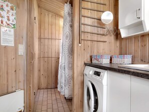 A compact, wooden-finished bathroom with a washing machine, a towel rack, and a shower curtain. - 4 Star Holiday Home in Nexo (Nexø)