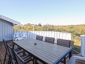 An outdoor patio with a wooden table and chairs, a white fence, and a view of the landscape. - 12 Person Holiday Home in Hjorring (Hjørring)