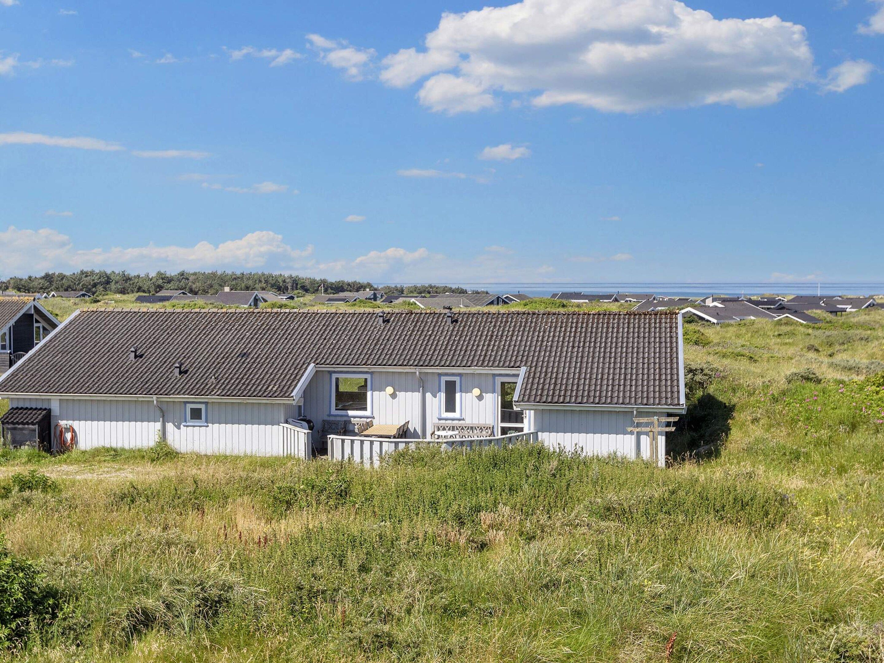 Uma casa à beira-mar com telhado inclinado, cercada por um campo gramado e vista para o mar.