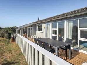Un área de comedor al aire libre techada con una mesa, sillas, una terraza de madera y barandilla blanca.
