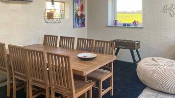 A dining area with a wooden table and chairs, a window with a view of a field, and a wall-mounted air conditioner.