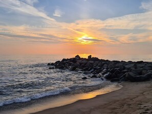 Una playa con un rompeolas rocoso, olas y un atardecer.