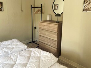 Un dormitorio con una cama, un aparador de madera, un espejo y un perchero.