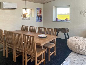 Un comedor con mesa y sillas de madera, una ventana con vistas a un campo y un aire acondicionado de pared.