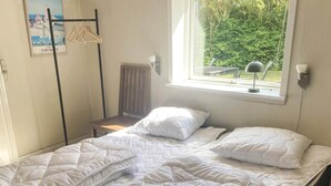 A single bed with white bedding in a room with a window, a radiator, and a poster on the wall. - 4 Person Holiday Home in Lemvig (Lemvig)