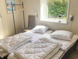 Una cama individual con ropa de cama blanca en una habitación con ventana, radiador y un cartel en la pared.