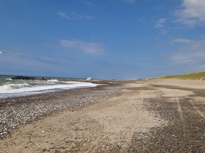 A beach with pebbles, a dirt path, and the ocean.