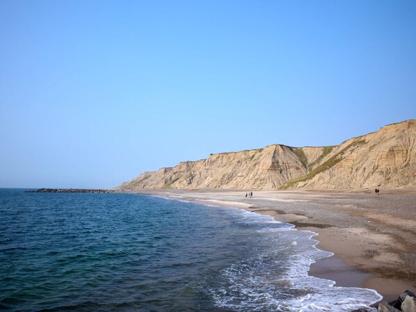 A beach with a clear sky, a rocky cliff, and a calm sea.