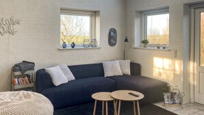 A cozy living room with a dark blue sofa, two round wooden side tables, a bookshelf, and a skylight above. - 4 Person Holiday Home in Lemvig (Lemvig)