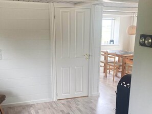A room with a white door, a dining area with wooden furniture, and a light-colored floor.