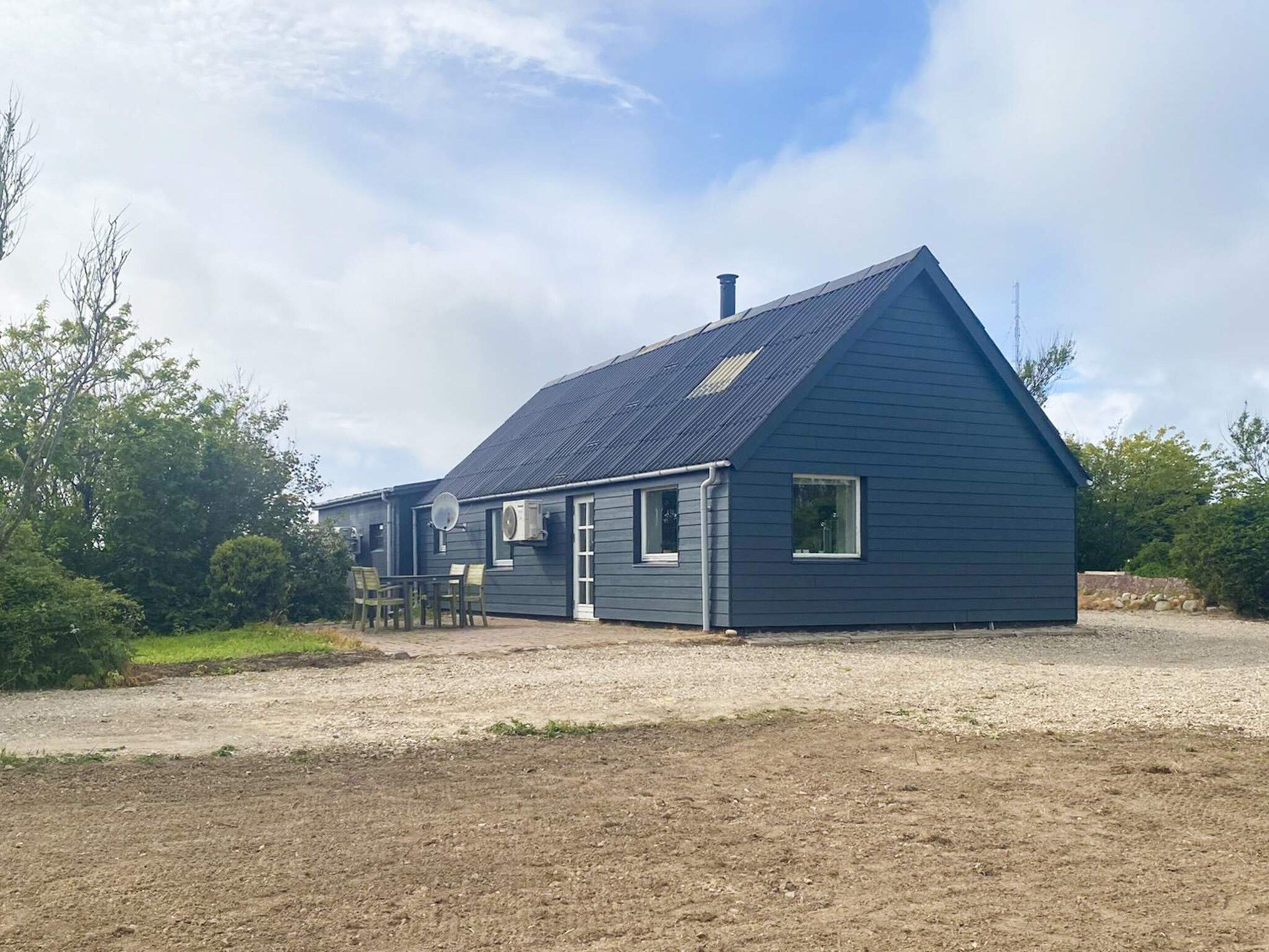 A single-story building with a sloped roof, a satellite dish, and a small porch with chairs.