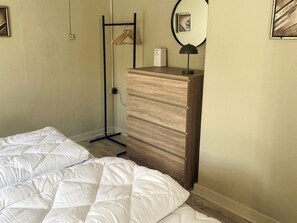 A bedroom with a bed, a wooden dresser, a mirror, and a hanging clothes rack.