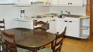A compact kitchen with white cabinets, a stove, a sink, and a coffee maker. There is a dining table with chairs. - 4 Person Holiday Home in Høyheimsvik (Luster)