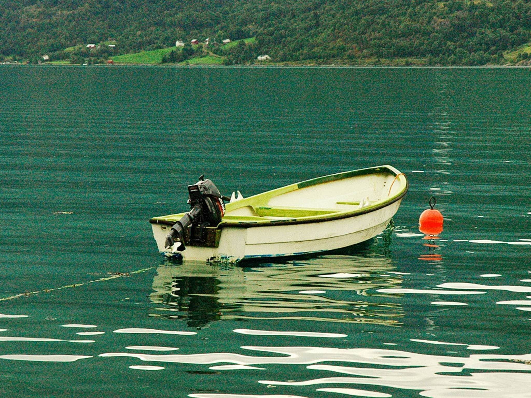 A small boat tied to an orange buoy on a calm lake with a forested shoreline in the background.