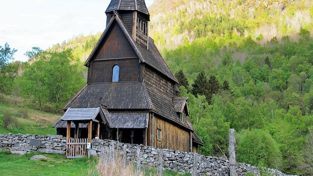 A wooden church with a steeply pitched roof and a bell tower, surrounded by lush greenery and a stone wall. - 4 Person Holiday Home in Høyheimsvik (Luster)