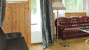 A room with a wooden floor, a red leather sofa, a patterned armchair, a floor lamp, and a window with curtains. - 4 Person Holiday Home in Høyheimsvik (Luster)