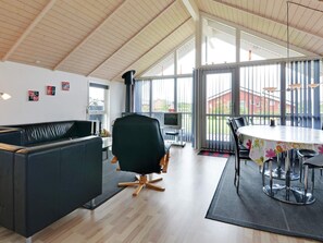 Un intérieur moderne avec un canapé en cuir noir, un fauteuil de bureau noir, une table ronde avec des chaises et une grande fenêtre donnant sur un immeuble rouge.
