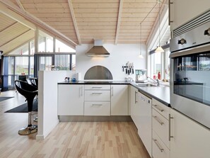 Une cuisine moderne dotée d’un grand îlot central, d’appareils électroménagers en acier inoxydable et offrant une vue dégagée par les fenêtres.