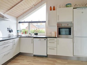 A modern kitchen with white cabinets, a dishwasher, an oven, and a refrigerator. There is a window providing natural light and a view of the outside.