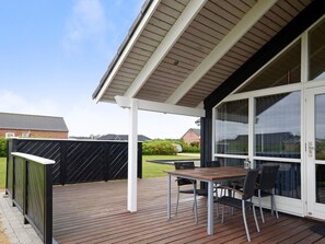 Une terrasse extérieure couverte, avec une table et des chaises, une porte-fenêtre coulissante et une vue sur le quartier.