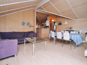A modern interior with a wooden ceiling, a purple sofa, a glass coffee table, and a dining area with white chairs and a blue tablecloth.