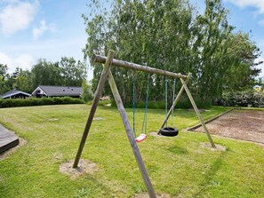 A wooden swing set with a tire swing in a grassy yard with trees and a house in the background. - Cozy Holiday Home in AsnÃ¦s near Fishing (Asnaes)