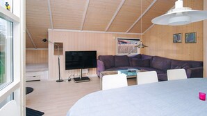 A modern living room with a large flat-screen TV, a purple sectional sofa, a glass coffee table, and a dining table with chairs. - Cozy Holiday Home in AsnÃ¦s near Fishing (Asnaes)