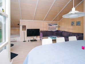 Uma sala de estar moderna com uma grande televisão de tela plana, um sofá seccional roxo, uma mesa de centro de vidro e uma mesa de jantar com cadeiras.
