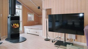 A modern room with a wood-burning stove, a bed, a TV, and a glass table. - Cozy Holiday Home in AsnÃ¦s near Fishing (Asnaes)