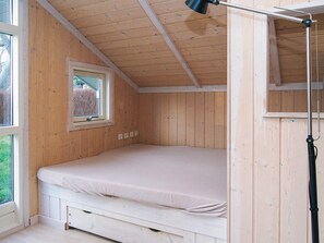 A small, wooden room with a single bed, a window, and a ceiling lamp.