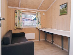 Um quarto pequeno com decoração em madeira, uma janela com cortinas, uma mesa e um sofá.
