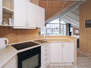 Een moderne keuken met witte kasten, een zwarte kookplaat en een groot raam dat voor natuurlijk licht zorgt.