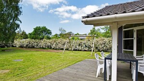 A wooden deck with outdoor furniture, a swing set, and a garden with a hedge. - Cozy Holiday Home in AsnÃ¦s near Fishing (Asnaes)