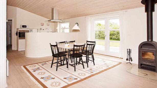 A modern kitchen with a central island, a dining area with a round table and chairs, and a wood-burning stove. - 4 Star Holiday Home in Hemmet (Hemmet)