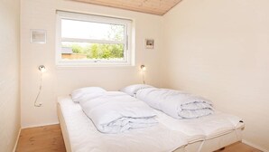 A room with a single bed, two bedside lamps, a window, and a wooden ceiling.