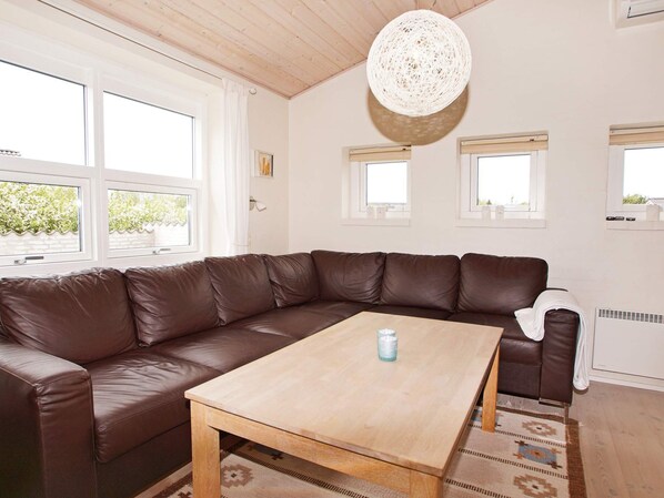 A modern living room with a brown leather sectional sofa, a wooden coffee table, and a woven light fixture.