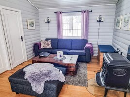 Una sala de estar acogedora con un sofá azul, una mesa de centro de madera, un reposapiés mullido y una estufa antigua.