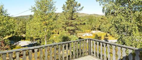 A wooden deck with a railing overlooking a forested area with trees and a rocky landscape.