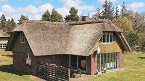 A thatched-roof cottage with a brick exterior, a wooden fence, and a grassy yard. - 8 Person Holiday Home in Blavand (Blavand)