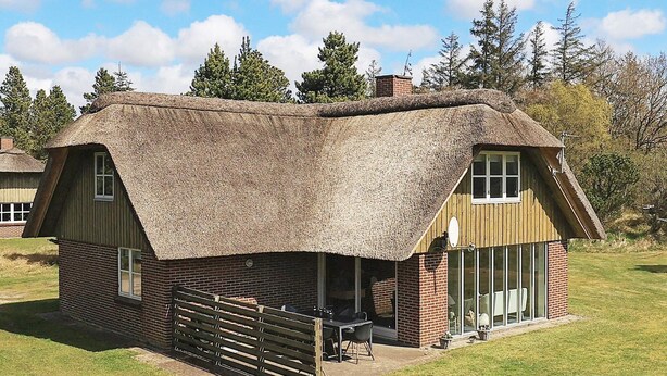A thatched-roof cottage with a brick exterior, a wooden fence, and a grassy yard.