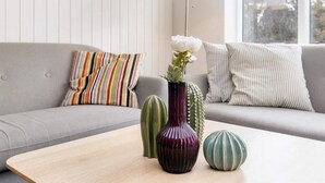 A modern living room with a grey sofa, colorful striped pillow, a tall floor lamp, and a wooden coffee table with decorative vases and a cactus.