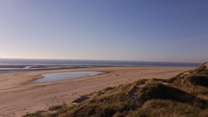 A coastal landscape with a sandy beach, grassy dunes, and a clear sky. - 8 Person Holiday Home in Blavand (Blavand)