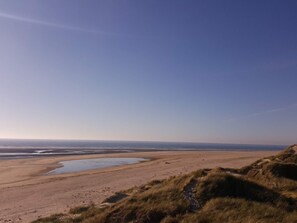 Ett kustlandskap med en sandstrand, gräsklädda sanddyner och en klar himmel.