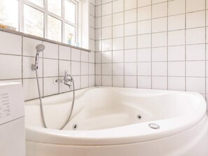 A white bathtub with a shower head and faucet, tiled walls, and a window with a view of trees. - 8 Person Holiday Home in Blavand (Blavand)