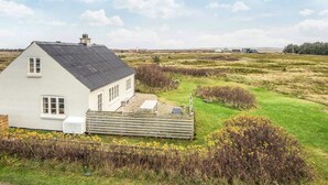 A white house with a sloped roof, a fenced yard, and a view of the surrounding landscape. - 6 Person Holiday Home in Harboore (Harboore)